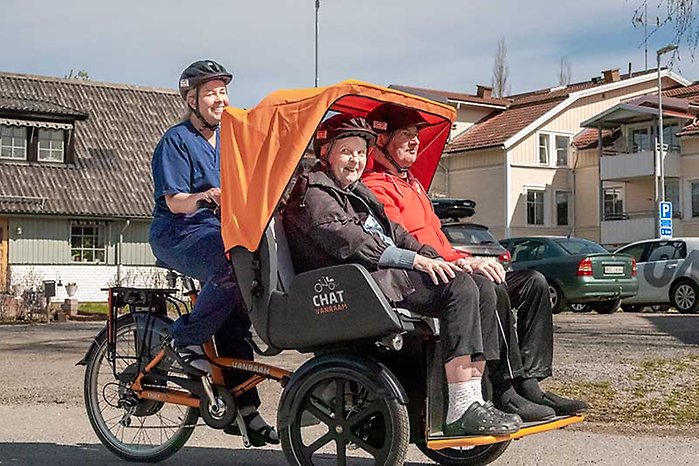 Personal på vård- och omsorgsboende skjutsar en dam och en herre i en passagerarcykel gjord för två personer. Cykeln liknar en så kallad tuktuk-cykel.