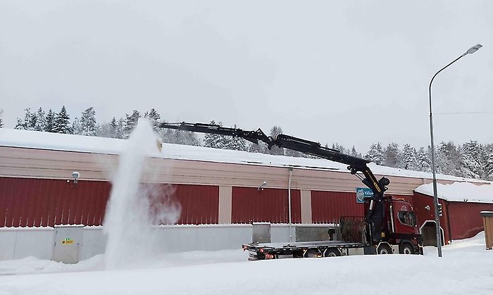 Snöbild med en lastbil med kranarm som sopar taket på en idrottsanläggning