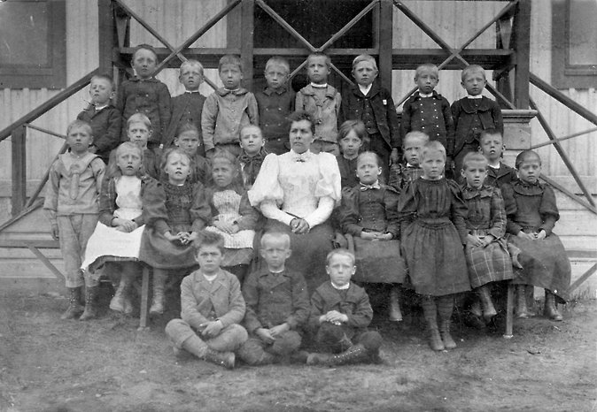 En skolklass med lärare och elever som sitter utanför skolan. svartvitt foto