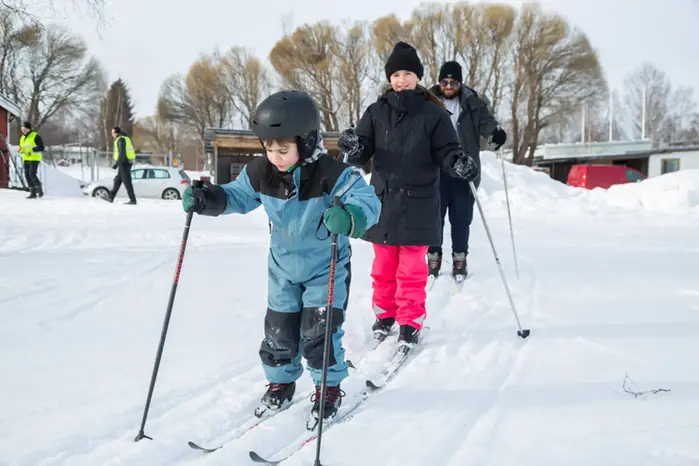 Två barn och en vuxen åker längdskidor. 