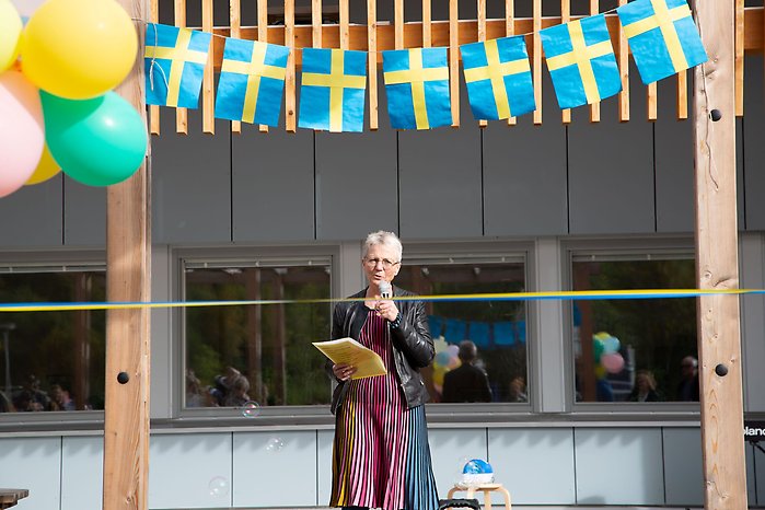 Kvinna som håller tal med svenska flaggor och ballonger i förgrunden.