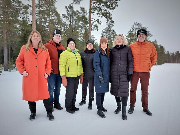 Grupp glada människor som står på en snötäckt mark och blickar in i kameran. 