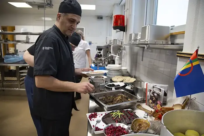 Manlig kock står vid bänk  i storkök där samiska rätter dukats fram