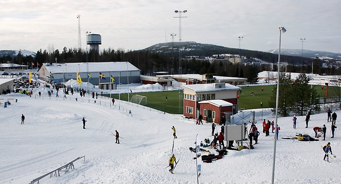 Vy över ett idrottsområde som visar både vintersport såsom skidåkning och en grön fotbollsplan med konstgräs